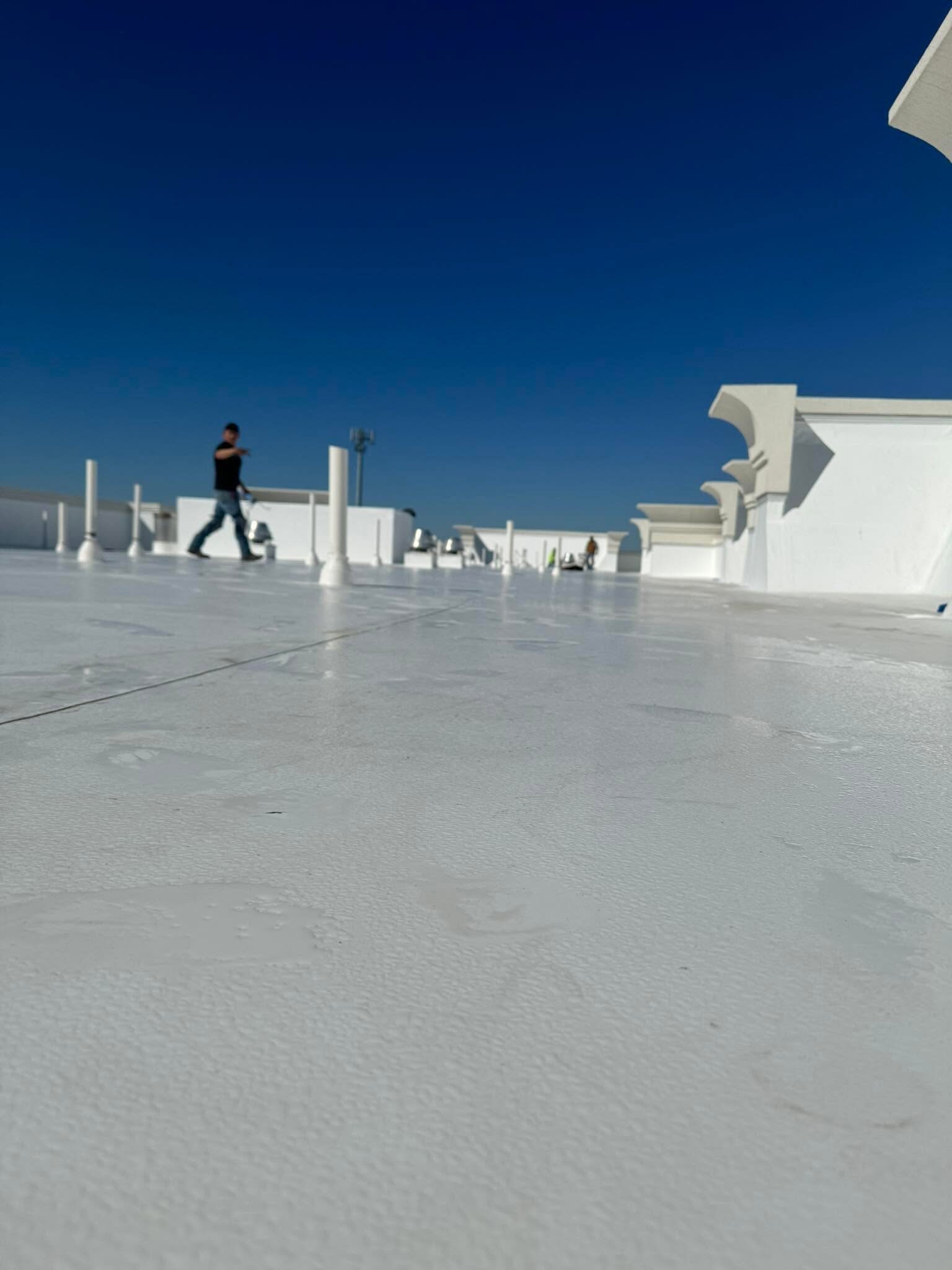Commercial flat roof with white membrane and a worker walking the roof for scale
