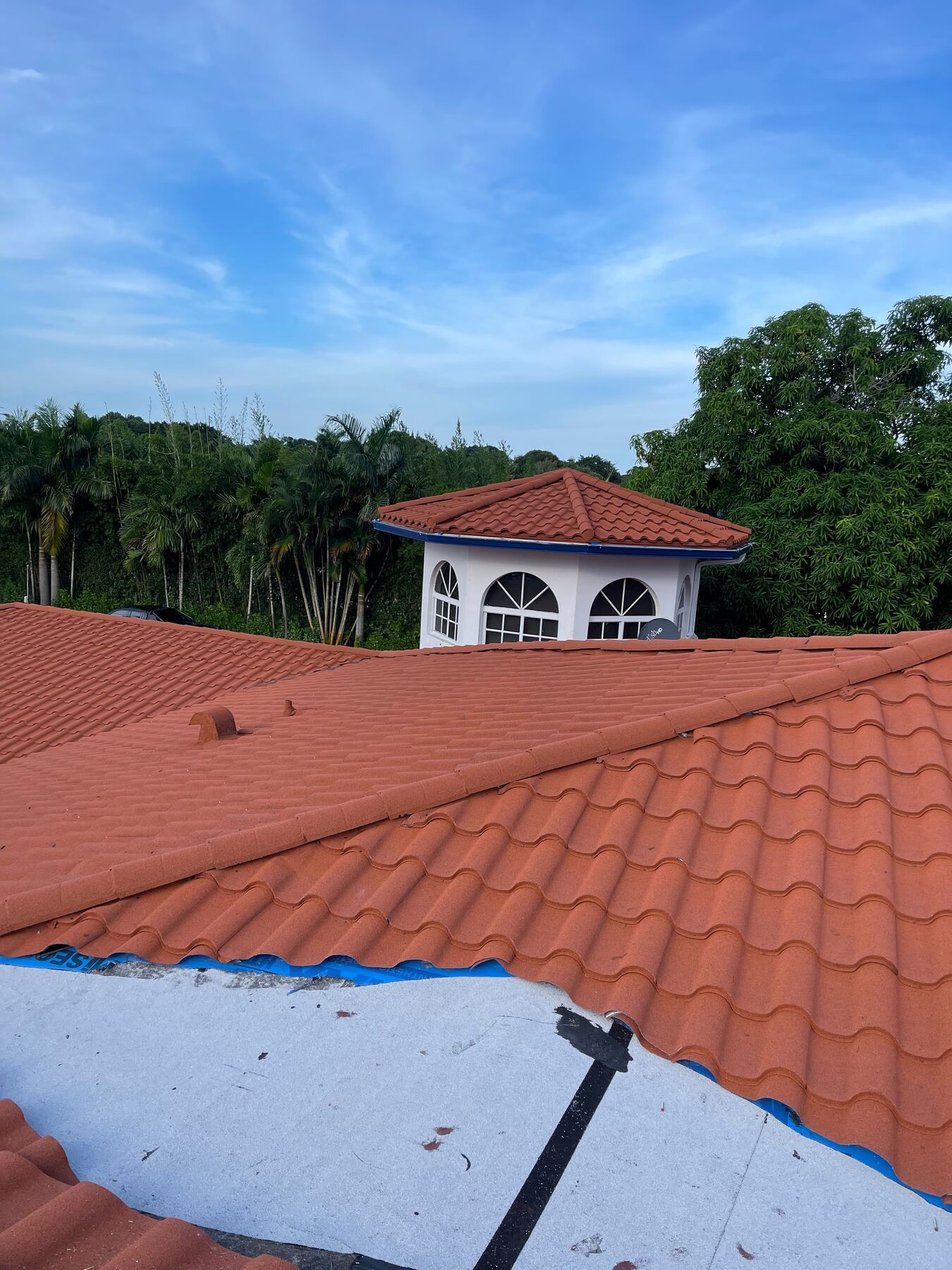 Tile roof mid-installation with blue self-adhering underlayment exposed before tile is laid